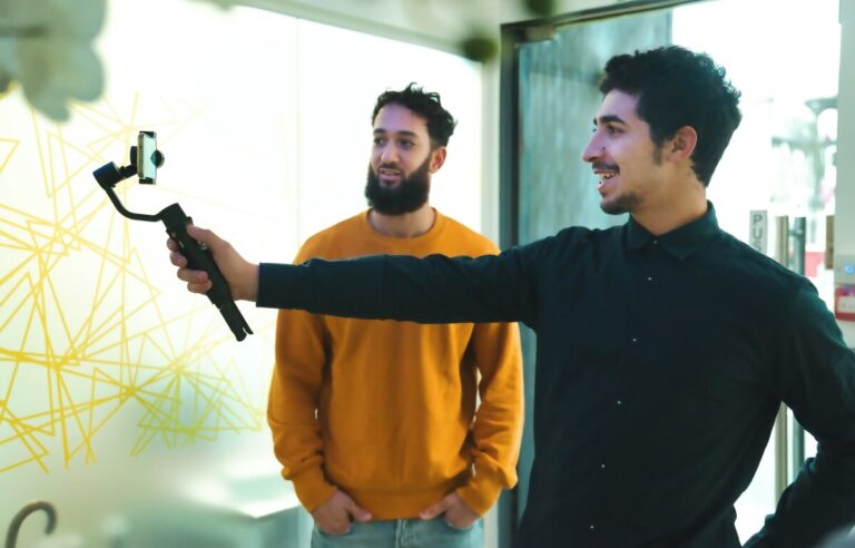 A man holds a camera whilst another stands watching